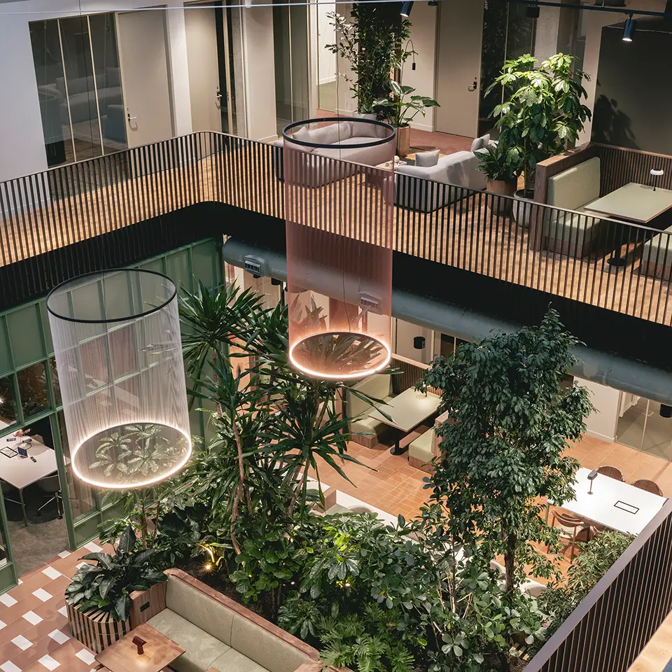 Aerial view down into the atrium showing hanging light fixtures, lush planting and seating areas