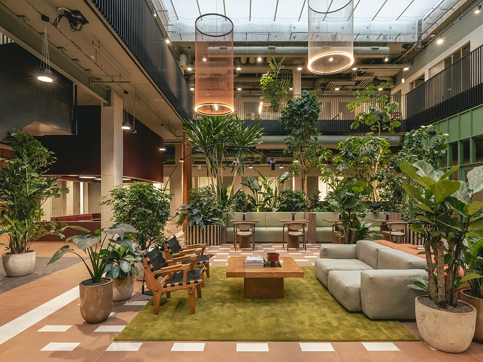Open atrium seating area with sofas and armchairs on a green rug surrounded by plants