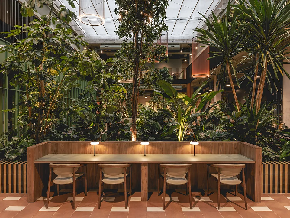 Communal workspace desk with individual lamps surrounded by lush greenery